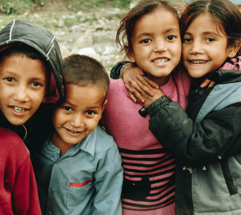 Four children standing closely next to each other, smiling and looking at the camera.