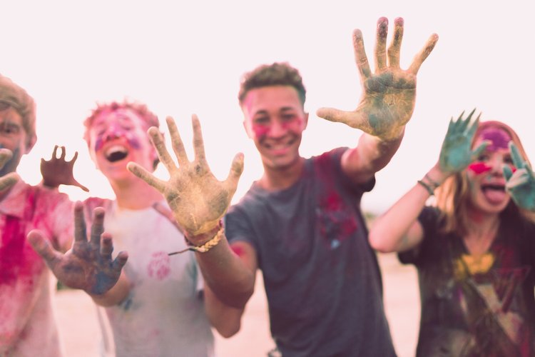 A group of four people covered in colorful paint, holding their painted hands in front of the camera.